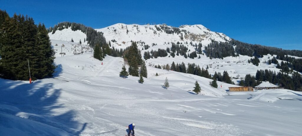 Im Vordergrund ein Skifahrer bei der Abfahrt, im Hintergrund windet sich die Strecke weiter hoch