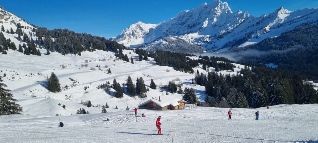 Im Vordergrund Skifahrer auf einer Piste vor einer Hütte