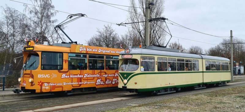 Von schräg vorne in voller Breite: Triebwagen 35 in beige mit grünen Streifen, Gelenkwagen 7756 im orangenen 1970er Schlagertram-Design