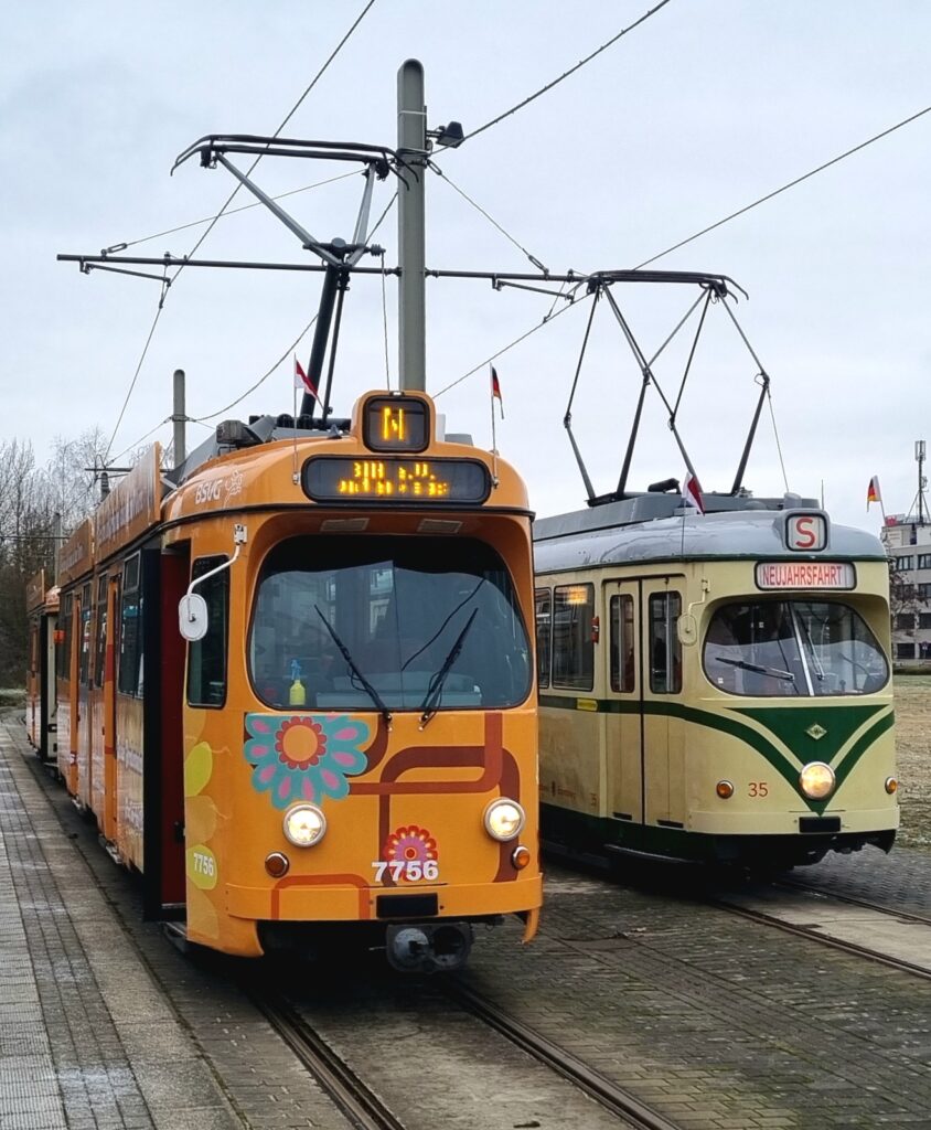 Von vorne: Gelenkwagen 7756 im orangenen 1970er Flower Power-Design neben Triebwagen 35 in beige mit grünen Streifen