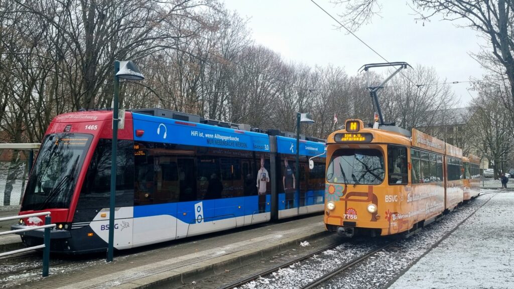 Von schräg vorne: Gelenkwagen 7756 im orangenen 1970er Flower Power-Design, Tramino 1465 in Dunkelrot, blau und weiß