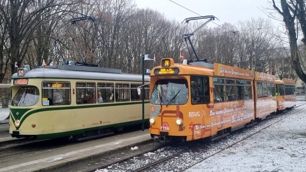 Von schräg vorne rechts: Triebwagen 35 in beige mit grünen Streifen neben Gelenkwagen 7756 im orangenen 1970er Flower Power-Design