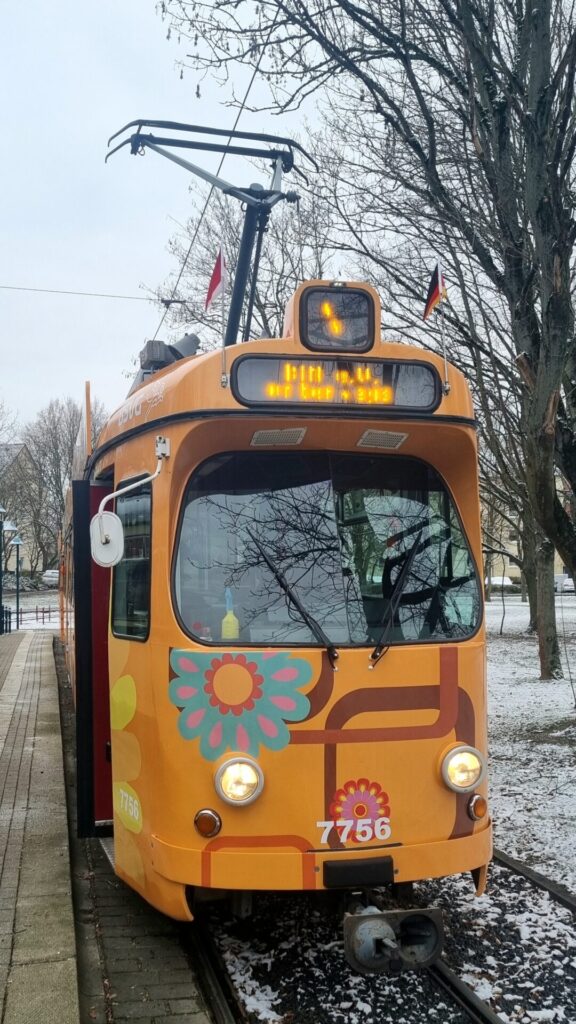 Von vorne, im orangenen 1970er Flower Power-Design, die digitale Linienanzeige und das Fahrtziel sind schlecht zu erkennen