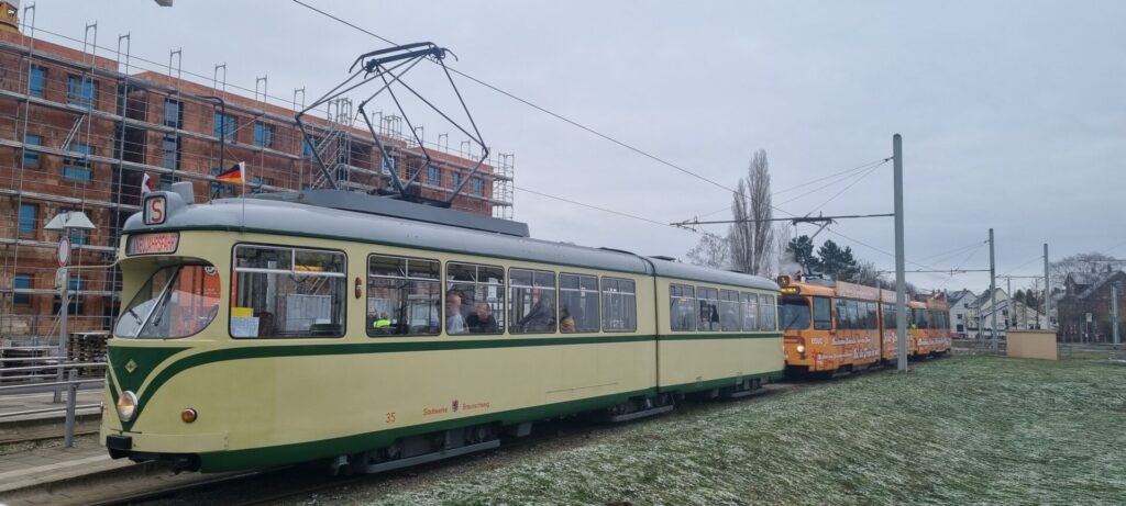 Von schräg vorne rechts und breit, Triebwagen 35 beige mit grünen Streifen, Gelenkwagen 7756 im orangenen 1970er FlowerPower-Motiv