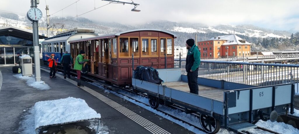 Ein Mitarbeiter steht auf dem Flachwagen, um Skier und Schlitten entgegen zu nehmen