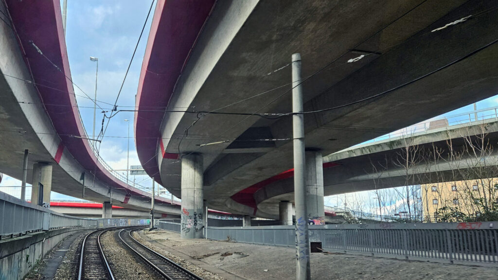 Zwei Straßenbahngleise, die aufsteigen und nach einer Rechtskurve zwischen den beiden Straßenbrücken eingefädelt und über den Rhein geführt werden